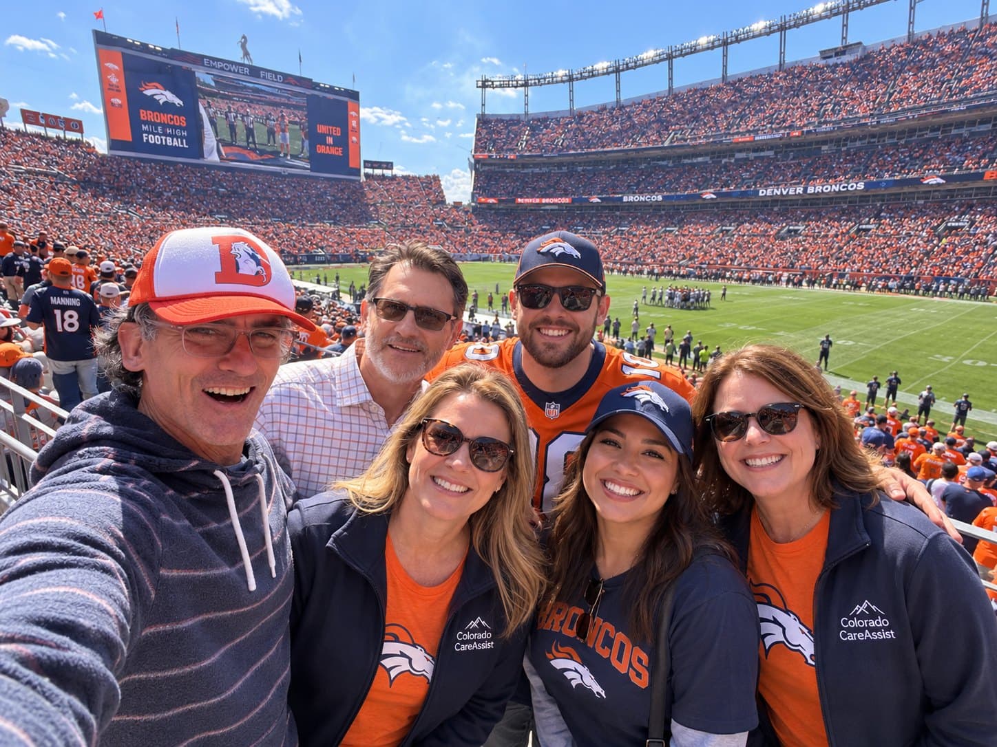 Colorado CareAssist team members together at a Denver Broncos game at Empower Field, several wearing Colorado CareAssist jackets